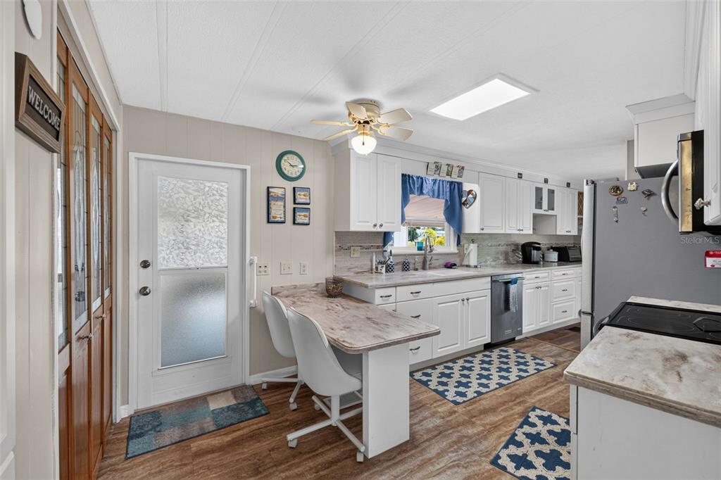 A kitchen features white cabinets, a breakfast bar, stainless steel appliances, and wood-look flooring — 240 LA COSTA, NORTH PORT, FL