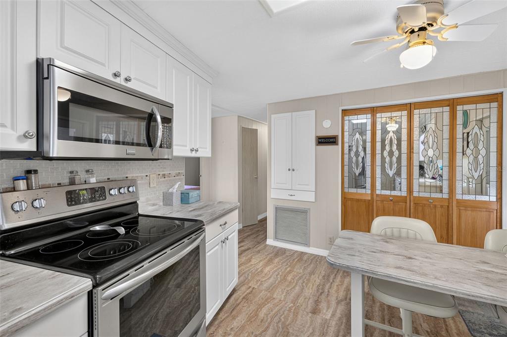 A kitchen features white cabinets, stainless steel appliances, and a dining table near glass-paneled doors — 240 LA COSTA, NORTH PORT, FL