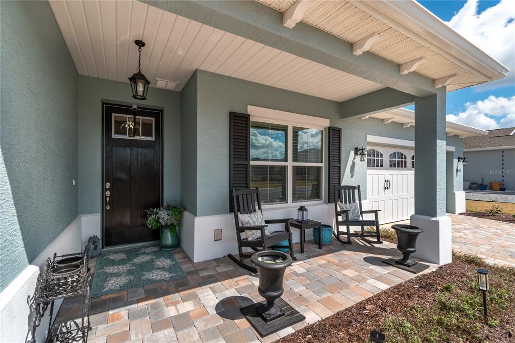 A covered front porch features a paver floor, two rocking chairs, and a dark front door — 10307 SW 96TH LANE, OCALA, FL