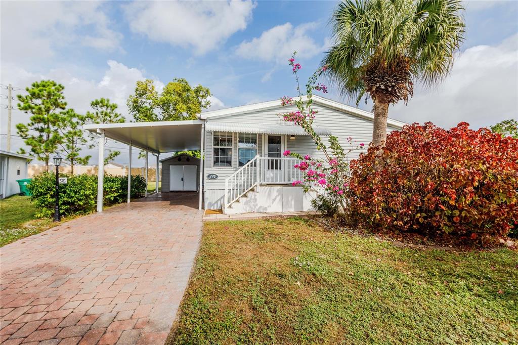 A light gray manufactured home features a brick driveway, a carport, and a palm tree — 2100 KINGS HIGHWAY UNIT 376, PORT CHARLOTTE, FL
