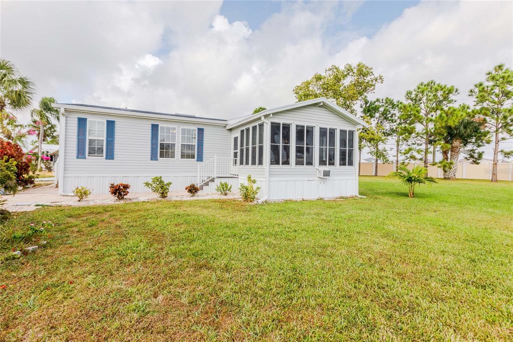 A light-colored mobile home features a screened-in porch and blue shutters on a grassy lot — 2100 KINGS HIGHWAY UNIT 376, PORT CHARLOTTE, FL