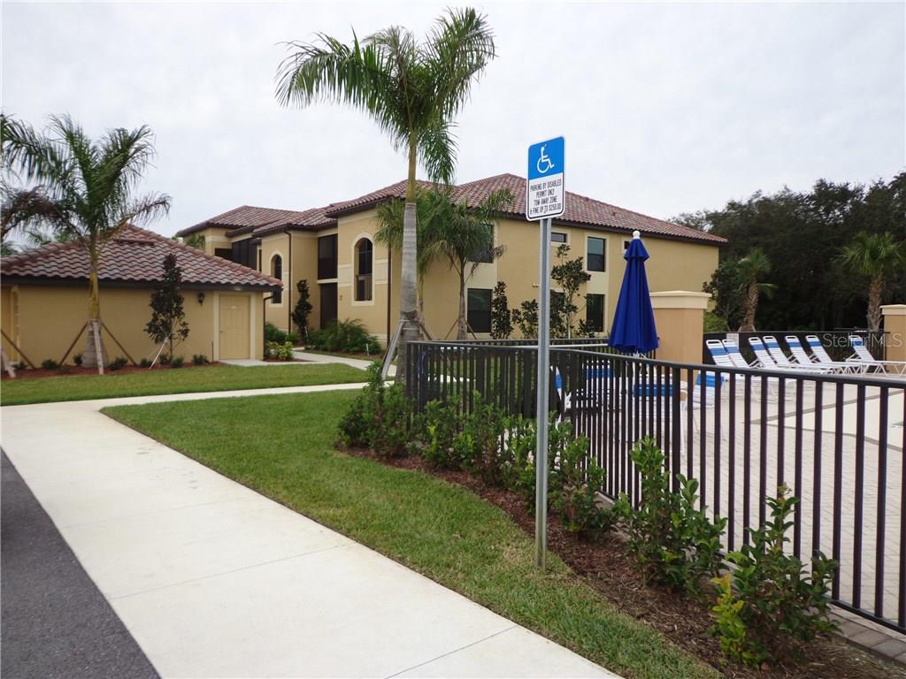An exterior view of a multi-story apartment building with a pool area and palm trees — 6715 GRAND ESTUARY TRAIL UNIT 106, BRADENTON, FL