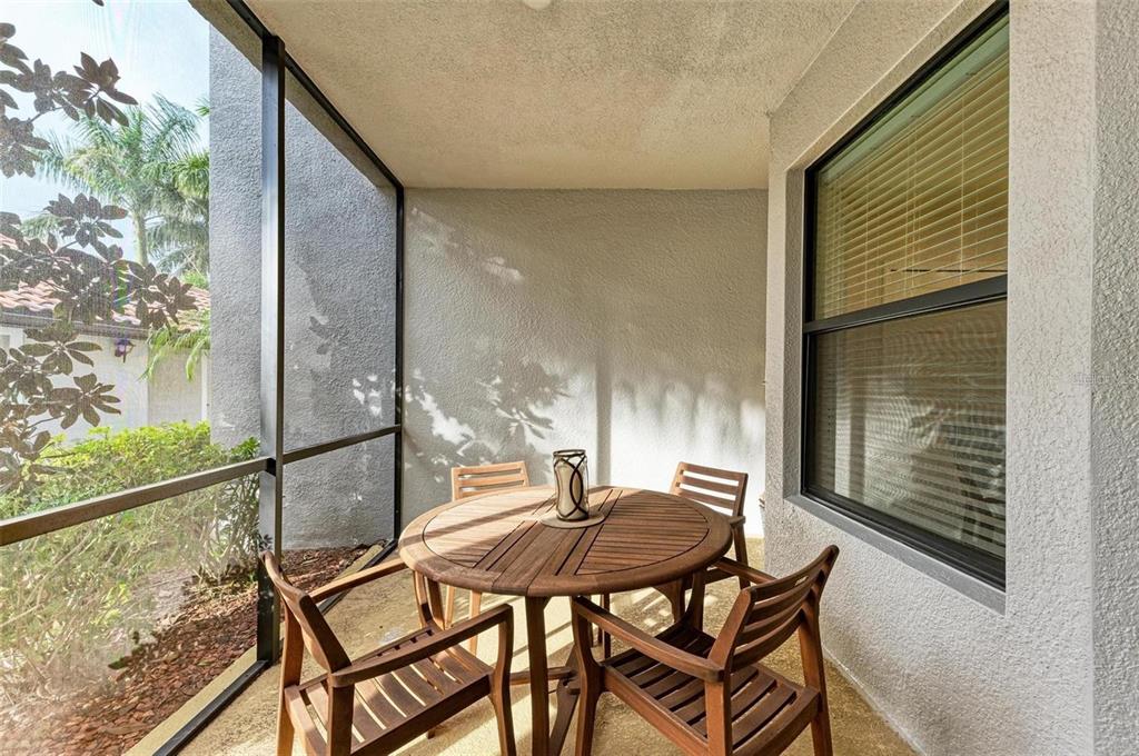 A screened-in patio features a round wooden table with four chairs on a concrete floor — 6715 GRAND ESTUARY TRAIL UNIT 106, BRADENTON, FL