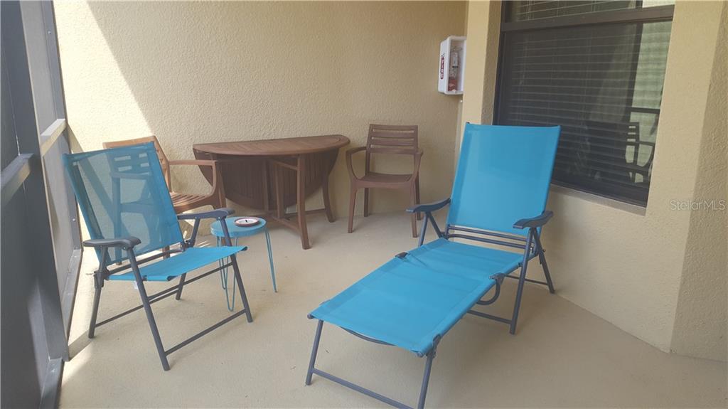 A screened-in patio features a wooden table, two chairs, and a blue lounge chair — 6715 GRAND ESTUARY TRAIL UNIT 106, BRADENTON, FL