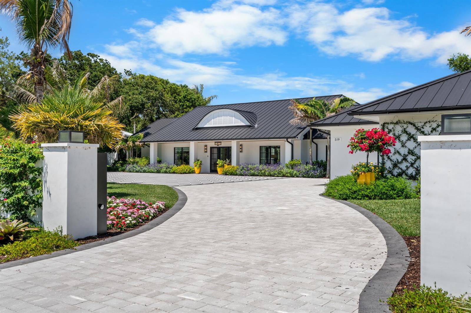 A paved driveway leads to a white house with a black metal roof and landscaping — VERO BEACH, FL