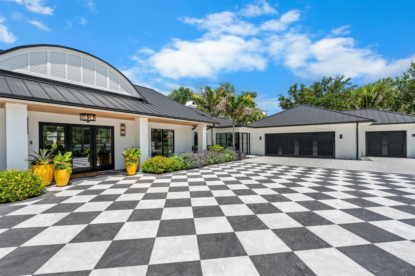 A modern white house features a black metal roof and a black-and-white checkered driveway — VERO BEACH, FL
