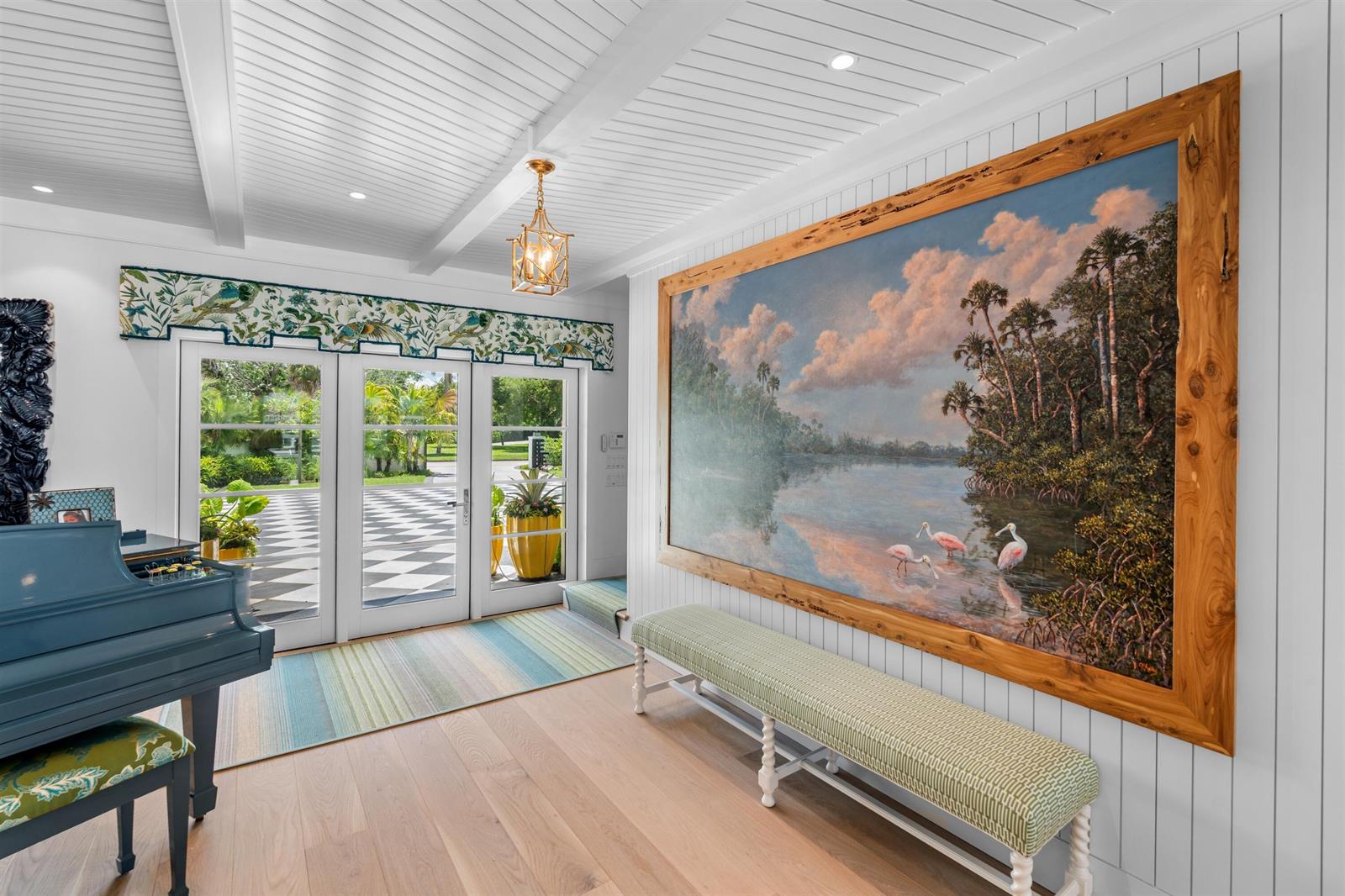 A bright entryway features a large landscape painting, a piano, and a long upholstered bench — VERO BEACH, FL