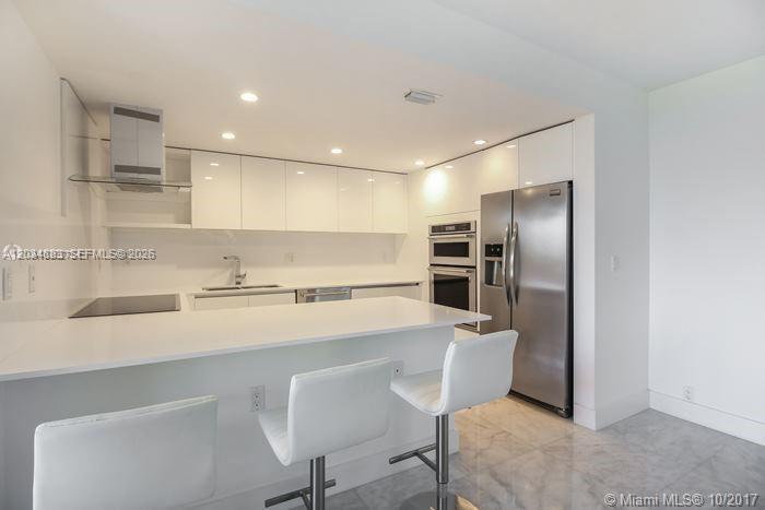 A modern kitchen features white cabinetry, stainless steel appliances, and a breakfast bar with stools — 101 Crandon Blvd # 474, Key Biscayne FL 33149, KEY BISCAYNE, FL