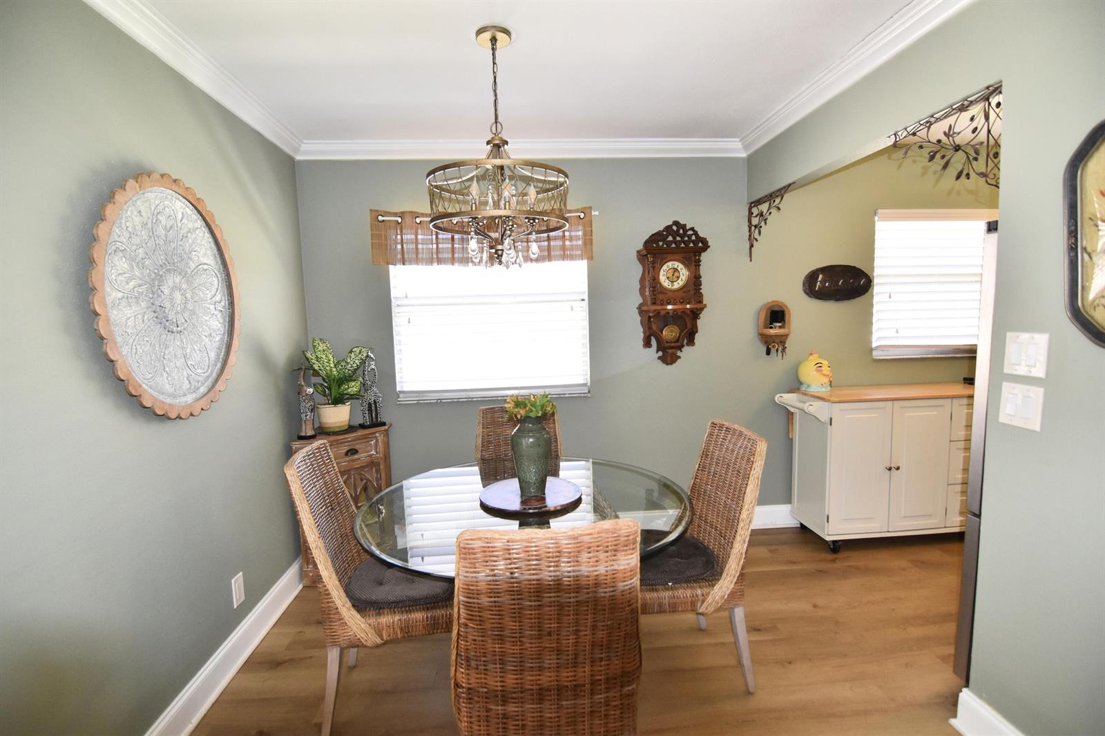 A dining room features a glass-topped table, wicker chairs, sage green walls, and wood flooring — 237 Saxony E, Delray Beach FL 33446, DELRAY BEACH, FL