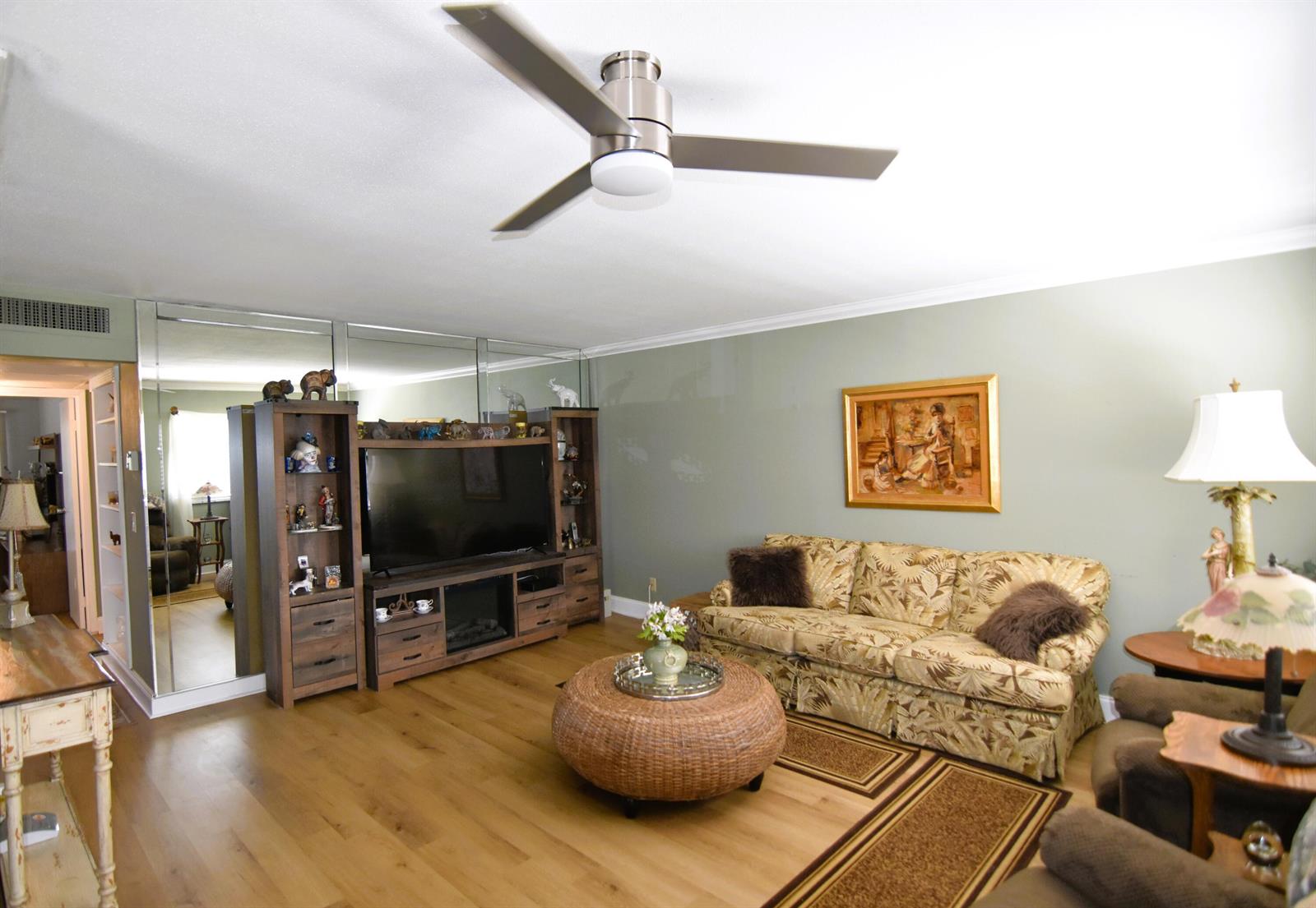 A living room with a ceiling fan, mirrored wall, wooden entertainment center, and patterned sofa — 237 Saxony E, Delray Beach FL 33446, DELRAY BEACH, FL