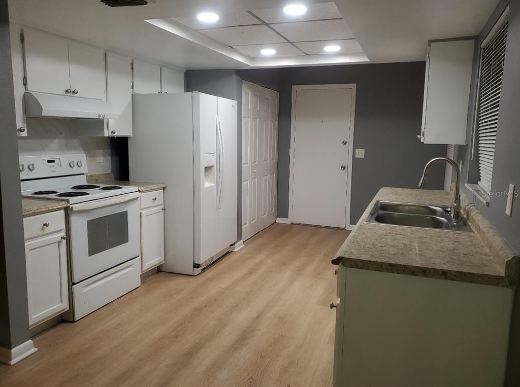 A kitchen features white cabinets, white appliances, light wood-look flooring, and a double-basin sink — 8211 CLERMONT STREET, TAMPA, FL