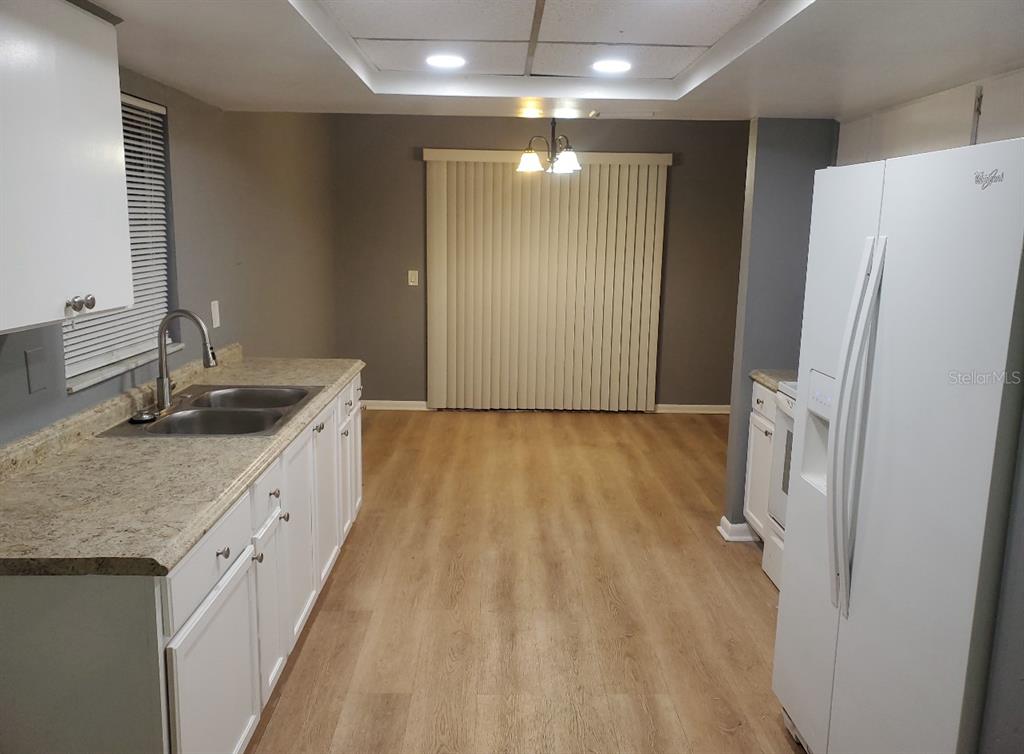 A kitchen with white cabinets, laminate countertops, and light wood-look flooring leads to a dining area — 8211 CLERMONT STREET, TAMPA, FL