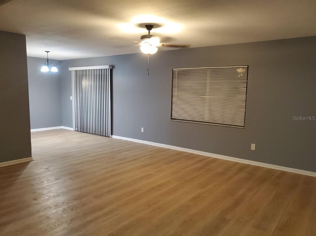An empty living room features gray walls, light wood-look flooring, a ceiling fan, and blinds — 8211 CLERMONT STREET, TAMPA, FL