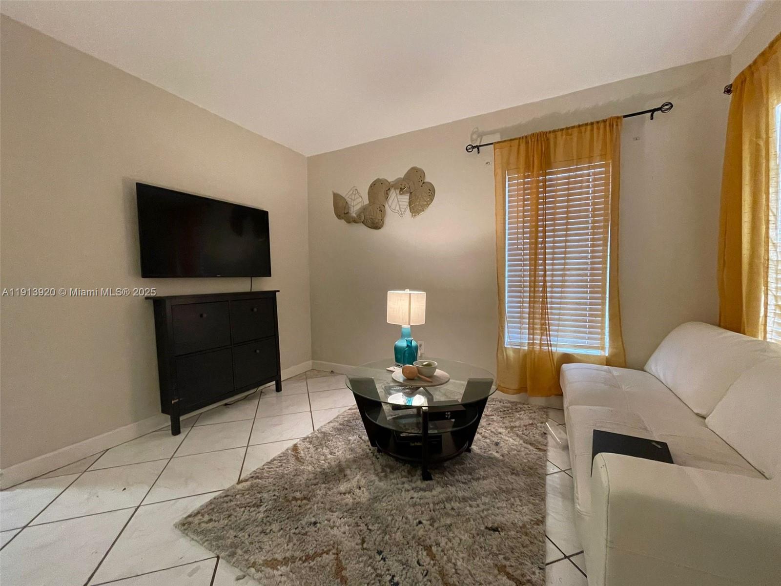 A living room features a white sofa, a glass coffee table, and a wall-mounted television — 55 NW 69th St, Miami FL 33150, MIAMI, FL