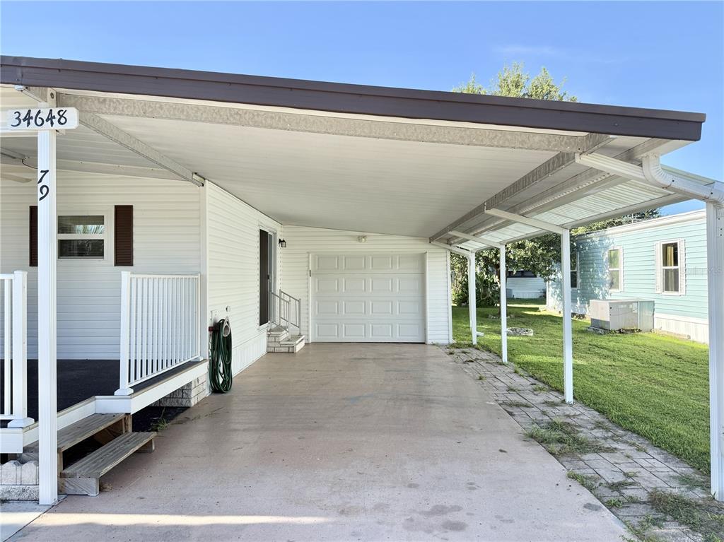 A white mobile home features a covered carport with a garage door and a side porch — 34648 SWEETPEA LANE, ZEPHYRHILLS, FL