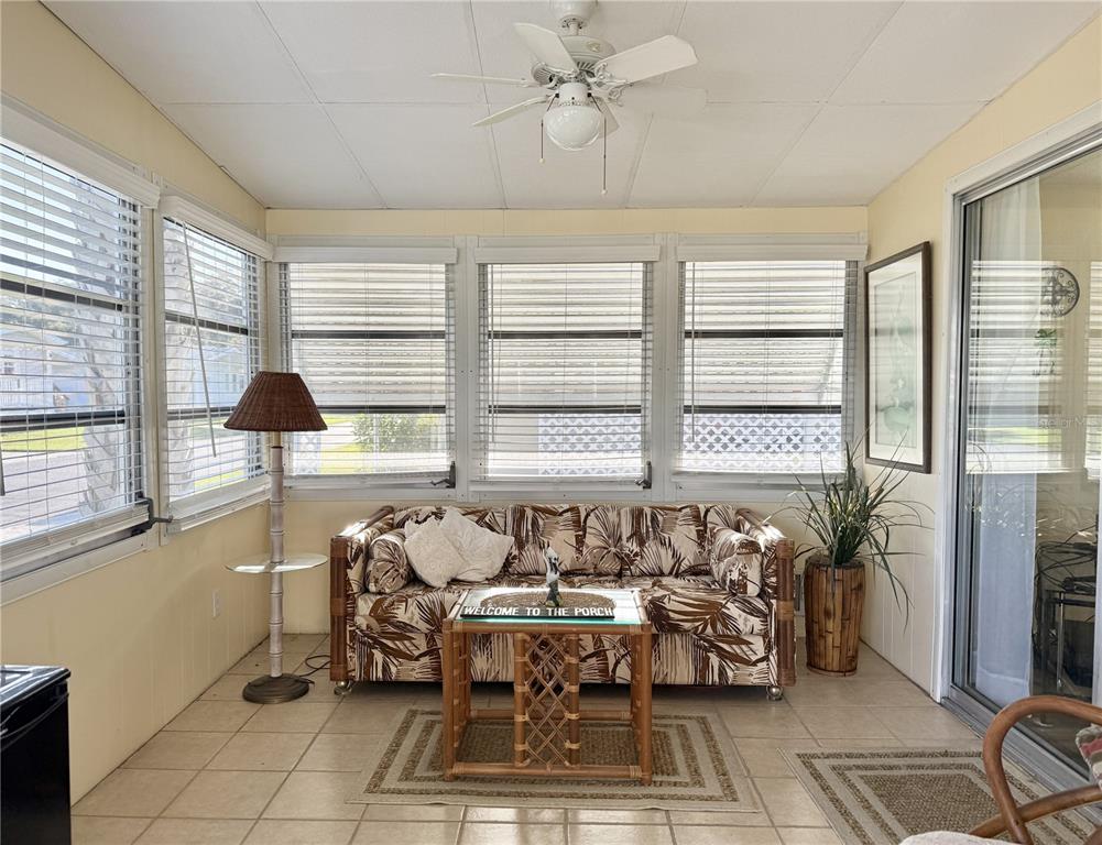 A sunroom features tile flooring, a tropical-print sofa, a ceiling fan, and large windows — 34648 SWEETPEA LANE, ZEPHYRHILLS, FL
