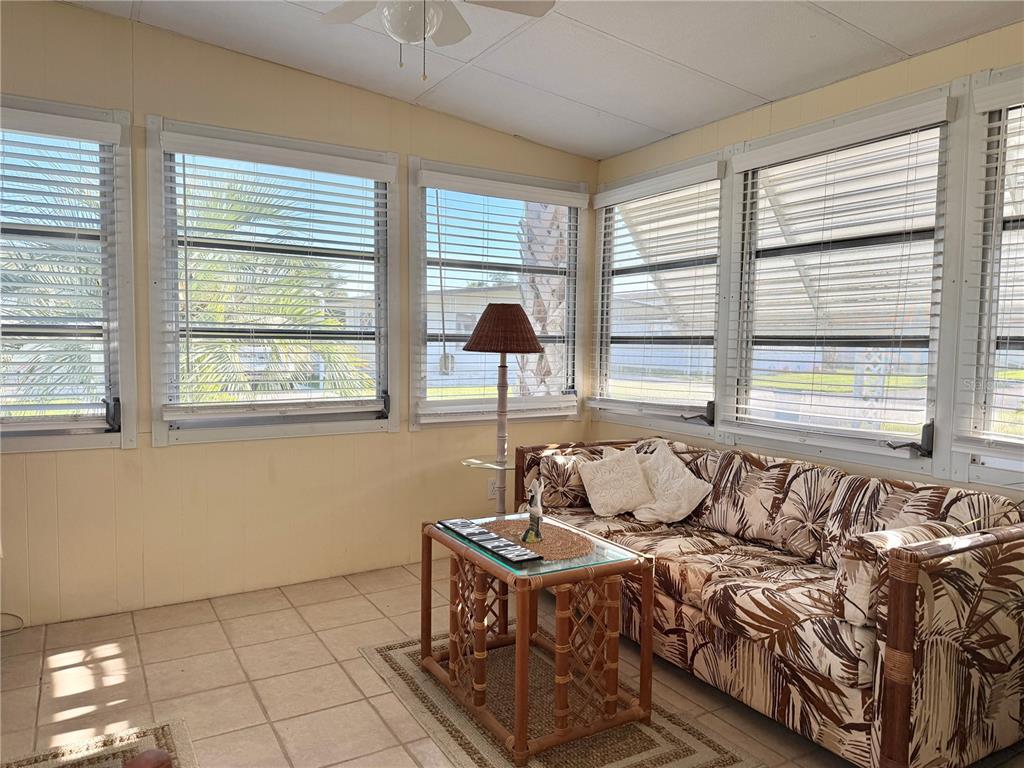 A sunroom features tile flooring, a rattan sofa, a glass-topped table, and multiple windows — 34648 SWEETPEA LANE, ZEPHYRHILLS, FL