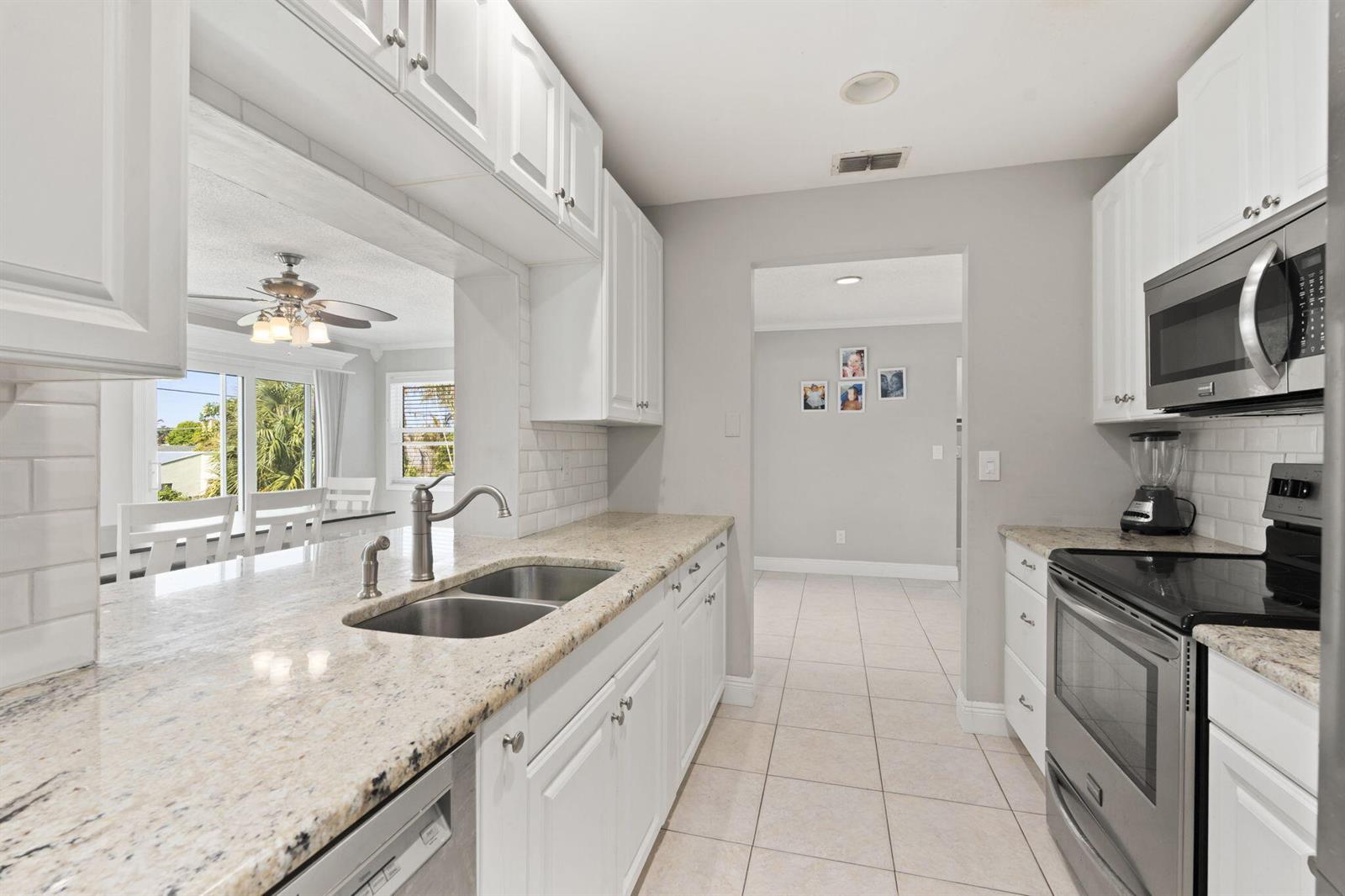 A kitchen with white cabinets, granite countertops, stainless steel appliances, and a double sink — 2268 NE 16th Court, Jensen Beach FL 34957, JENSEN BEACH, FL
