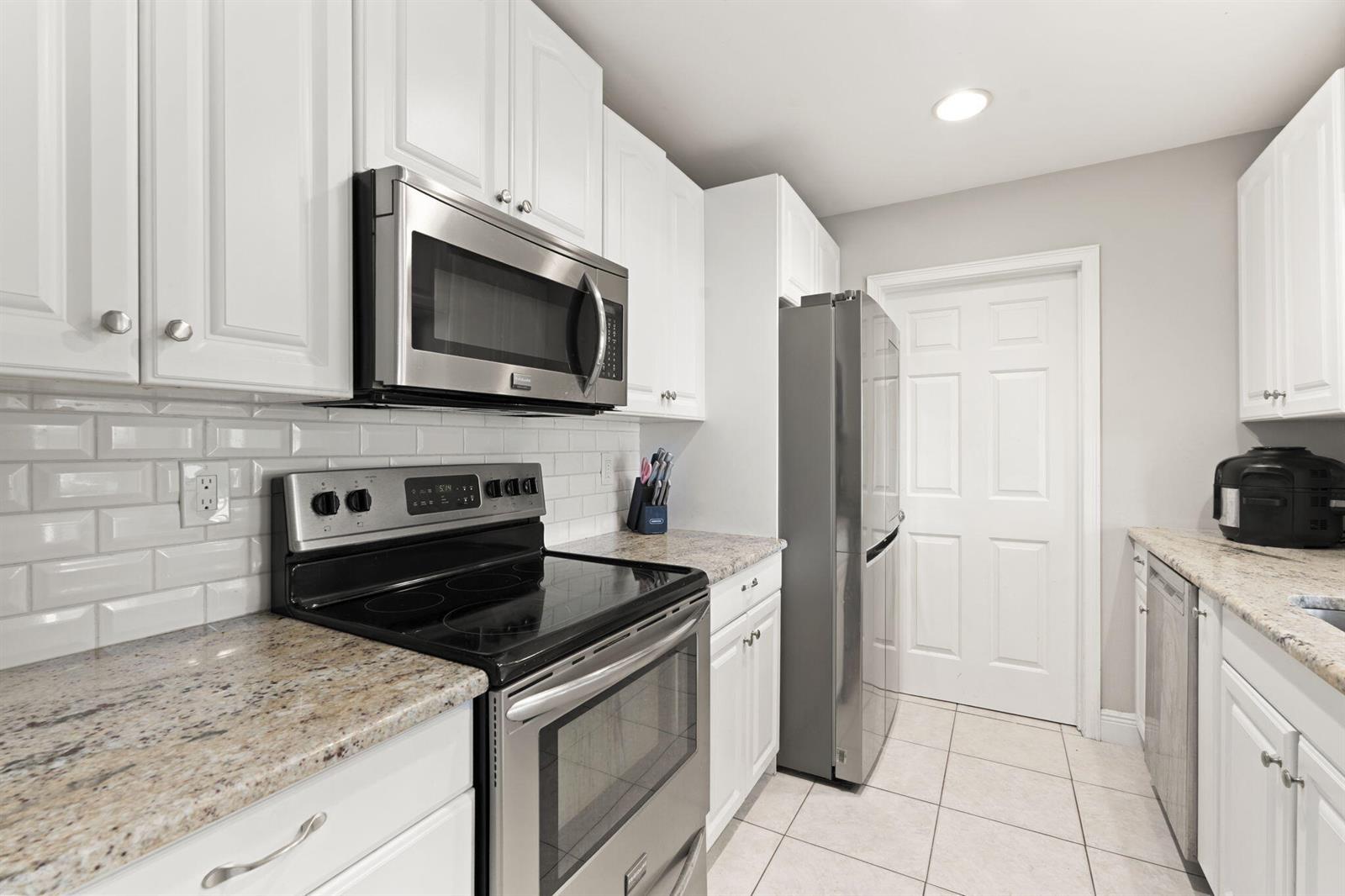 A kitchen with white cabinets, stainless steel appliances, granite countertops, and a subway tile backsplash — 2268 NE 16th Court, Jensen Beach FL 34957, JENSEN BEACH, FL