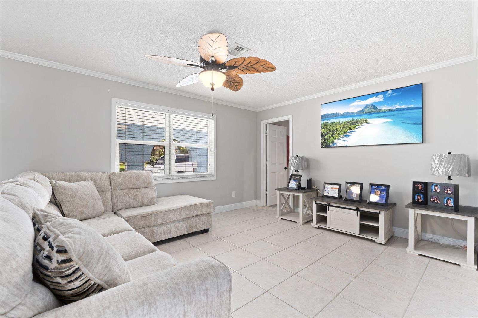 A living room features a beige sectional sofa, tile flooring, and a tropical ceiling fan — 2268 NE 16th Court, Jensen Beach FL 34957, JENSEN BEACH, FL