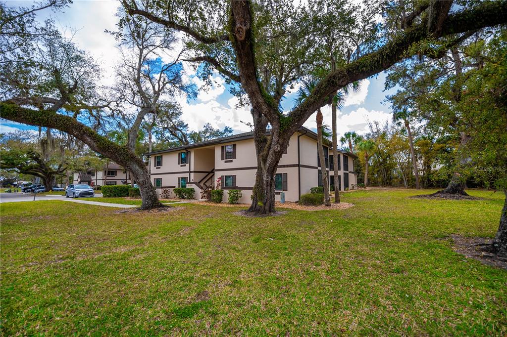 A two-story apartment building exterior surrounded by large oak trees and a grassy lawn — 19505 QUESADA AVENUE UNIT H101, PORT CHARLOTTE, FL