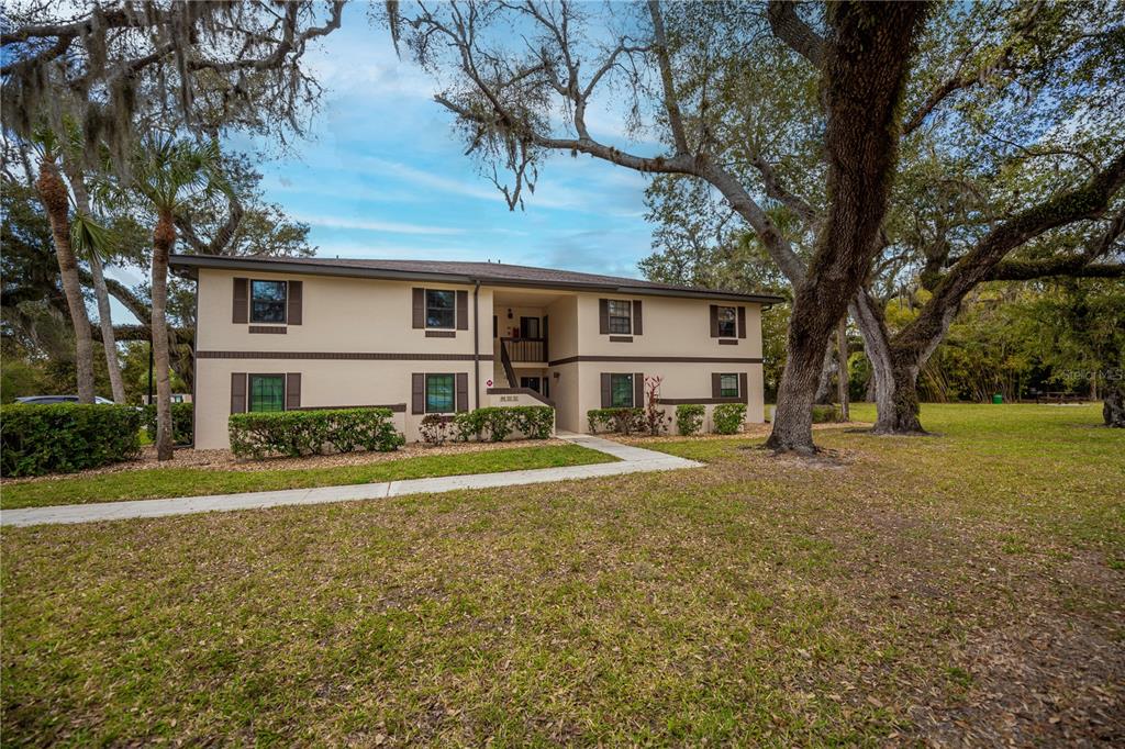 A two-story apartment building with tan stucco walls and dark brown trim sits on grass — 19505 QUESADA AVENUE UNIT H101, PORT CHARLOTTE, FL