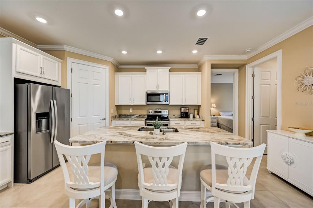 A kitchen features white cabinets, stainless steel appliances, a marble-topped island, and three white chairs — 113 VINADIO BOULEVARD, NOKOMIS, FL
