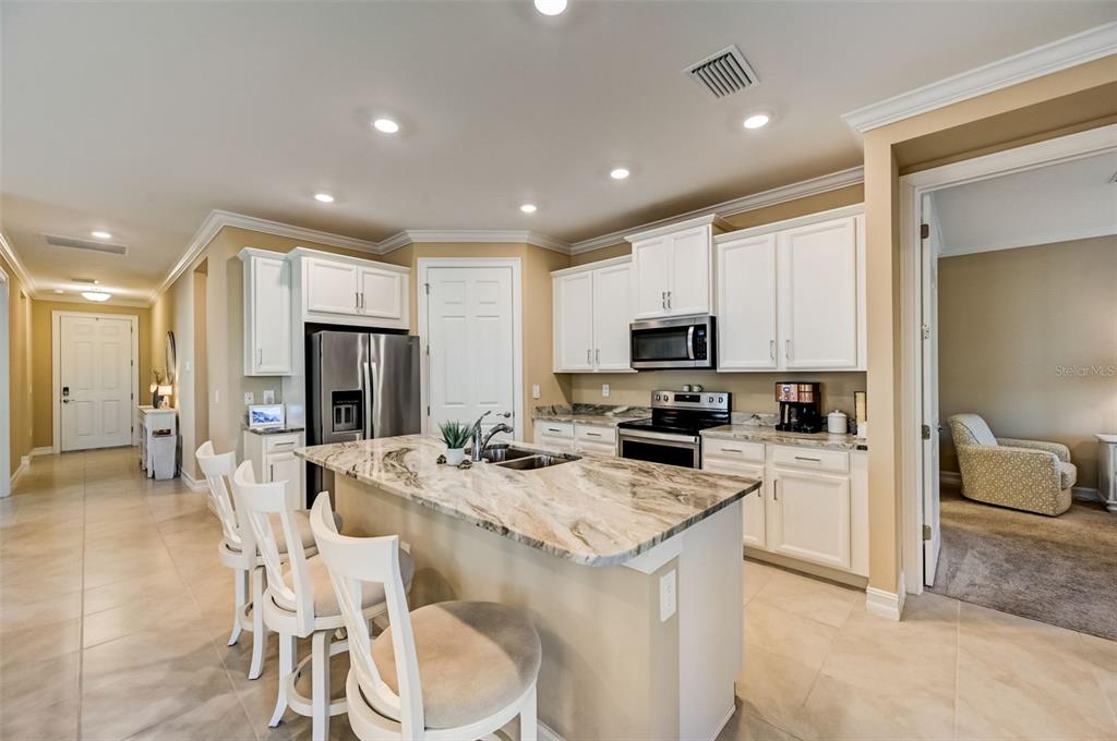 A kitchen features white cabinets, a stone-topped island with bar seating, and tile flooring — 113 VINADIO BOULEVARD, NOKOMIS, FL