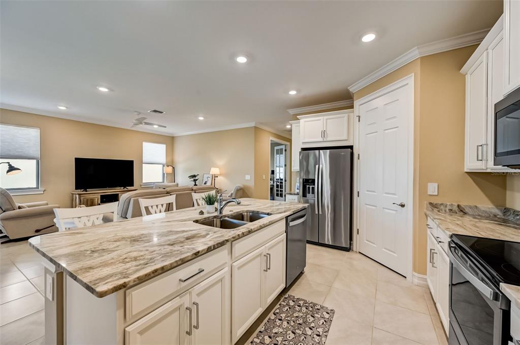 A kitchen with white cabinets and granite countertops overlooks an open-concept living area — 113 VINADIO BOULEVARD, NOKOMIS, FL