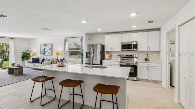 A modern kitchen with white cabinets, a large island, and bar stools overlooks a living area — 2245 BOLGER AVENUE, SPRING HILL, FL