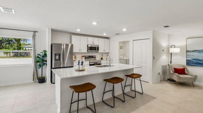 A modern kitchen features white cabinetry, a central island with bar stools, and stainless appliances — 2245 BOLGER AVENUE, SPRING HILL, FL