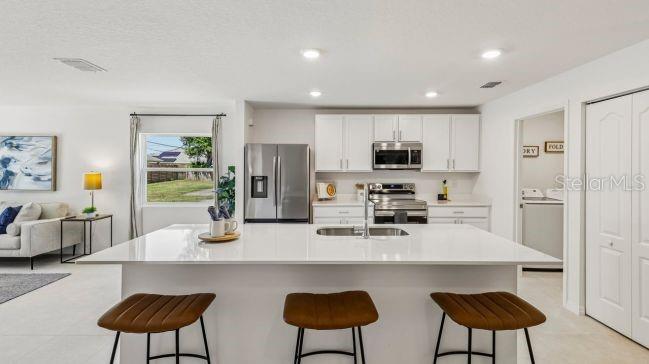 A modern kitchen features white cabinets, a large quartz island with three stools, and stainless appliances — 2245 BOLGER AVENUE, SPRING HILL, FL