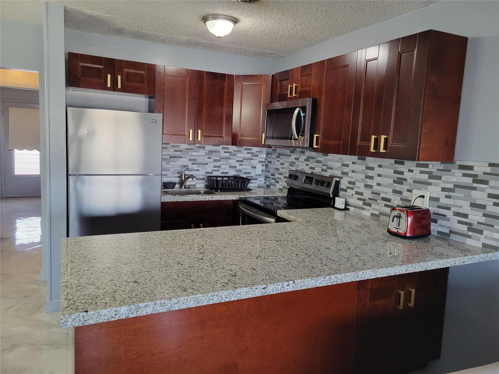 A kitchen features dark wood cabinets, granite countertops, a stainless steel refrigerator, and a tiled backsplash — 800 SW 11th Avenue # 17, Hallandale Beach FL 33009, HALLANDALE BEACH, FL