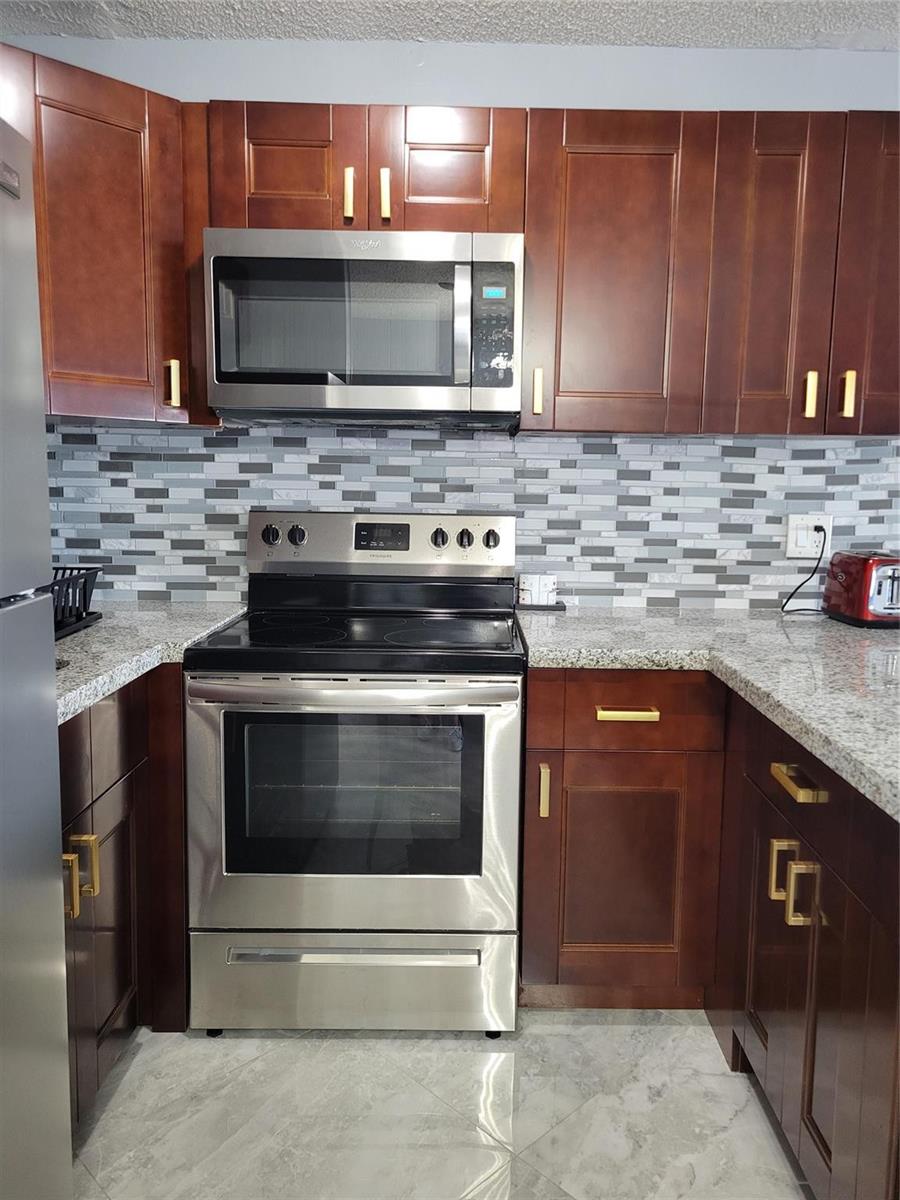 A kitchen featuring dark wood cabinets, stainless steel appliances, granite countertops, and a tiled backsplash — 800 SW 11th Avenue # 17, Hallandale Beach FL 33009, HALLANDALE BEACH, FL