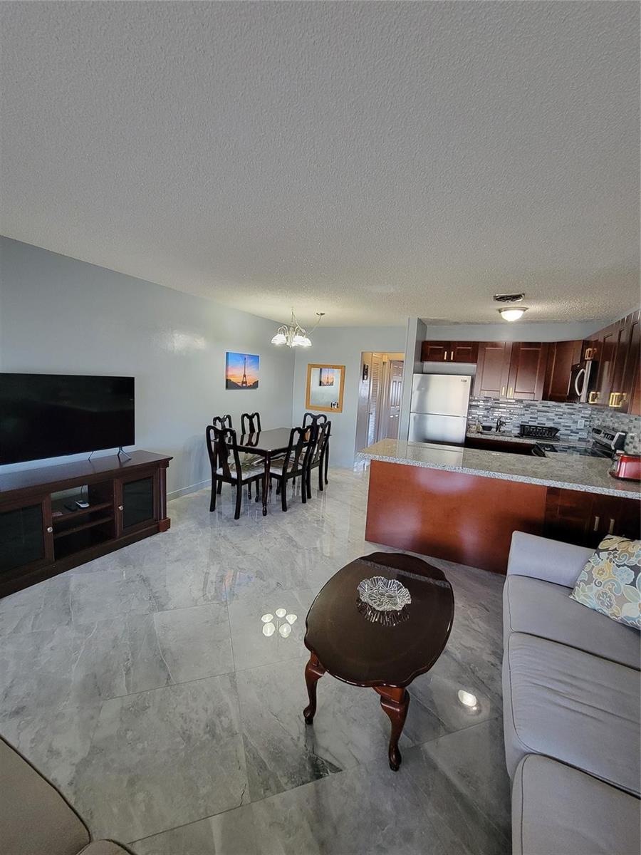 An open-concept living and dining area features tile flooring, dark wood cabinetry, and granite countertops — 800 SW 11th Avenue # 17, Hallandale Beach FL 33009, HALLANDALE BEACH, FL