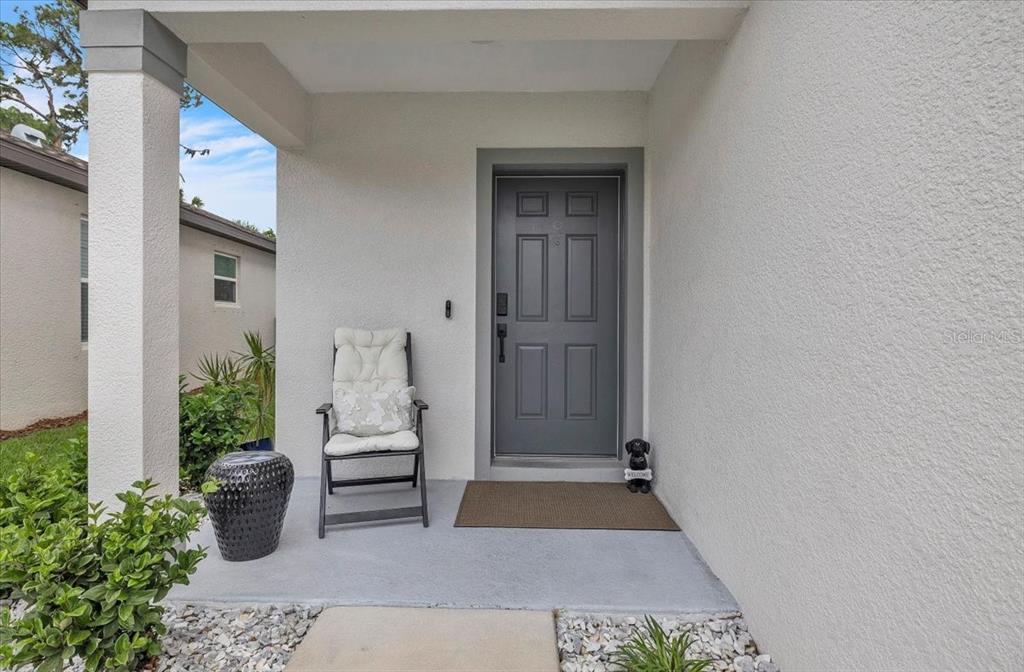 A gray front door with a chair and a small dog statue on a porch — 11783 MOONSAIL DRIVE, PARRISH, FL