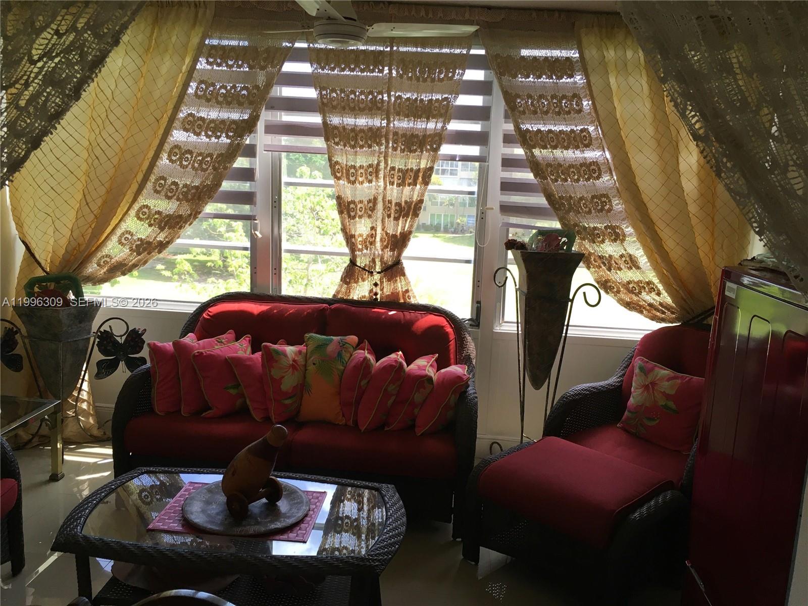 A sunroom features red wicker furniture, patterned throw pillows, and sheer curtains over large windows — 300 NE 26th Ave # 314, Boynton Beach FL 33435, BOYNTON BEACH, FL