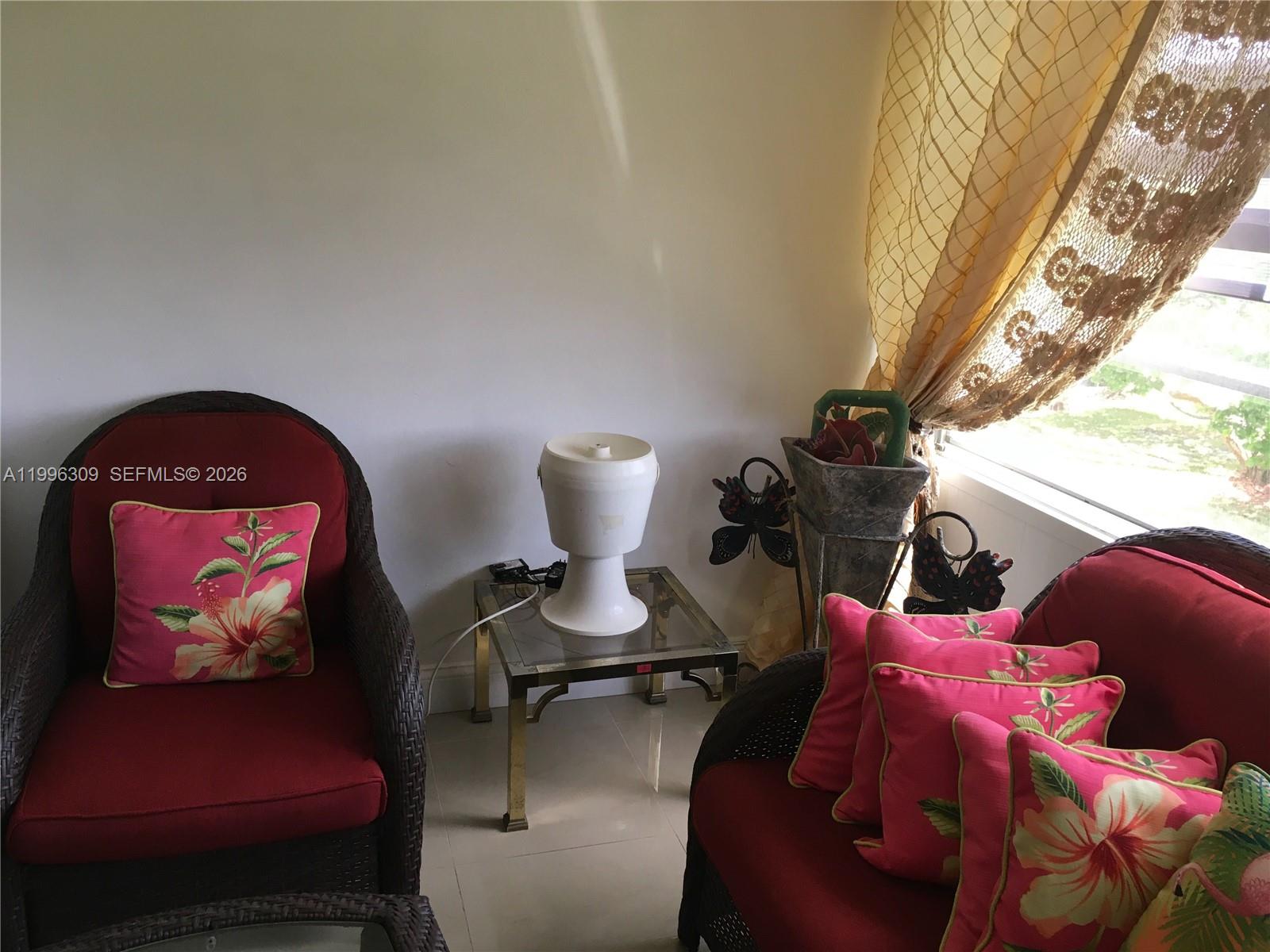 A sunroom features two wicker chairs with red cushions and floral pillows near a window — 300 NE 26th Ave # 314, Boynton Beach FL 33435, BOYNTON BEACH, FL