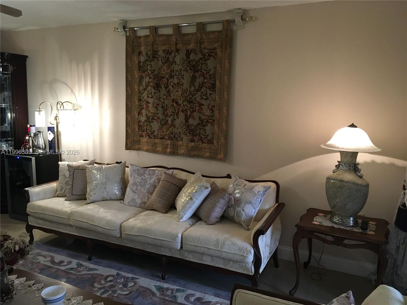 A living room features a cream sofa with decorative pillows, a wall tapestry, and lamps — 300 NE 26th Ave # 314, Boynton Beach FL 33435, BOYNTON BEACH, FL
