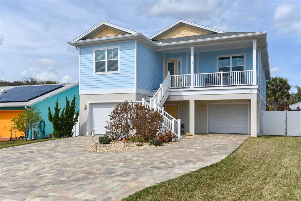 A two-story light blue house with a raised porch, two garages, and a paved driveway — 211 S 26TH STREET, FLAGLER BEACH, FL