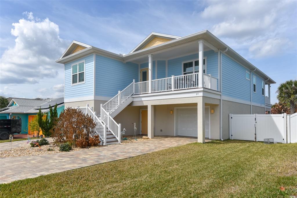 A light blue elevated house with a white porch, stairs, and a paved driveway — 211 S 26TH STREET, FLAGLER BEACH, FL