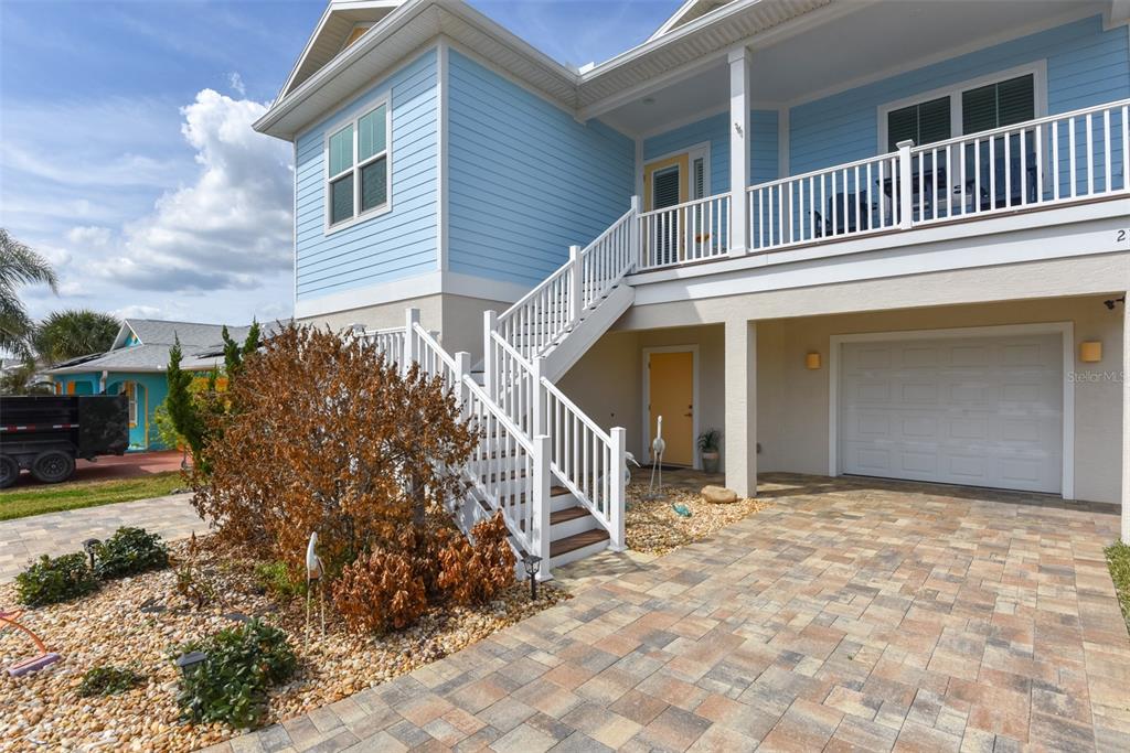 A light blue elevated house features a white staircase, a garage, and a paved driveway — 211 S 26TH STREET, FLAGLER BEACH, FL