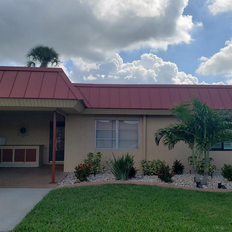 A single-story house exterior features a red metal roof, tan stucco walls, and landscaping — 4105 EL DORADO COVE, BRADENTON, FL