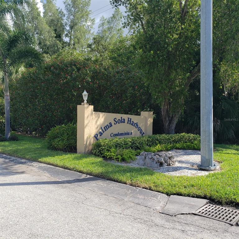 A tan monument sign for Palma Sola Harbour Condominium sits beside a road and trees — 4105 EL DORADO COVE, BRADENTON, FL