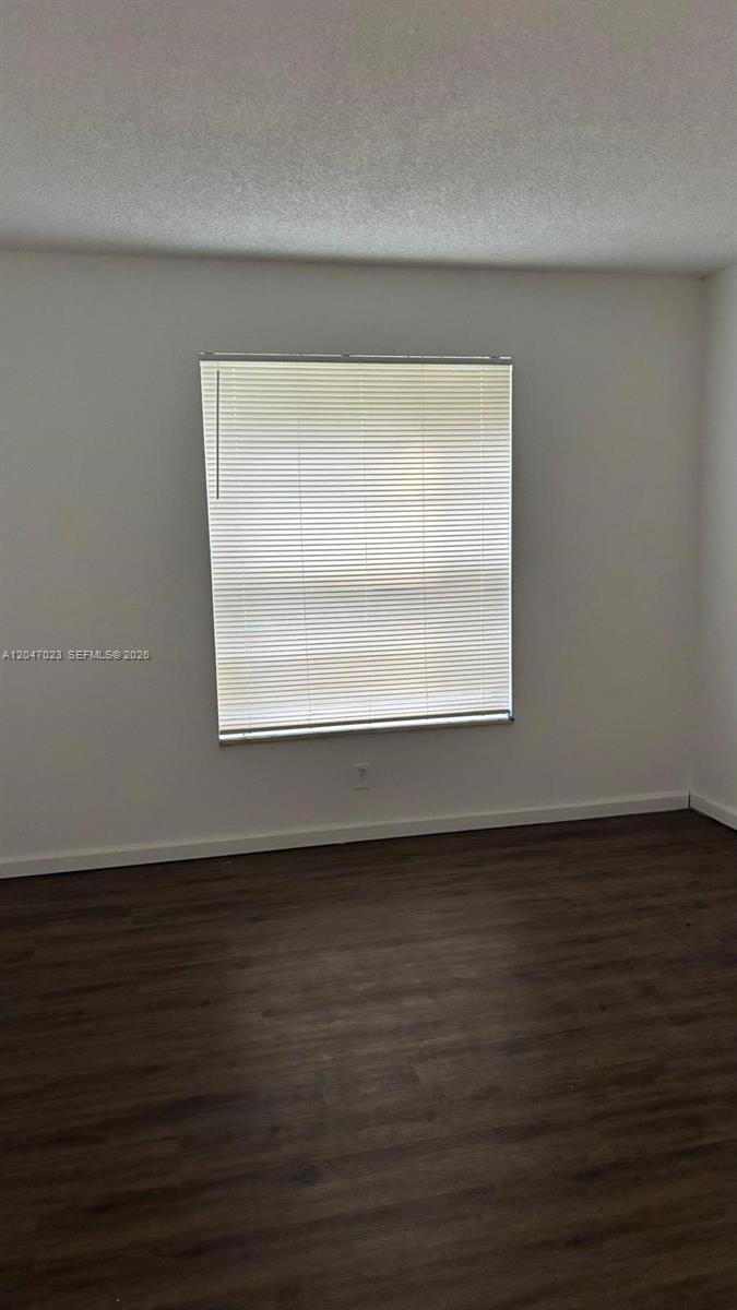 An empty room features white walls, dark wood-look flooring, and a window with blinds — 411 Executive Center Dr # 203, West Palm Beach FL 33401, WEST PALM BEACH, FL