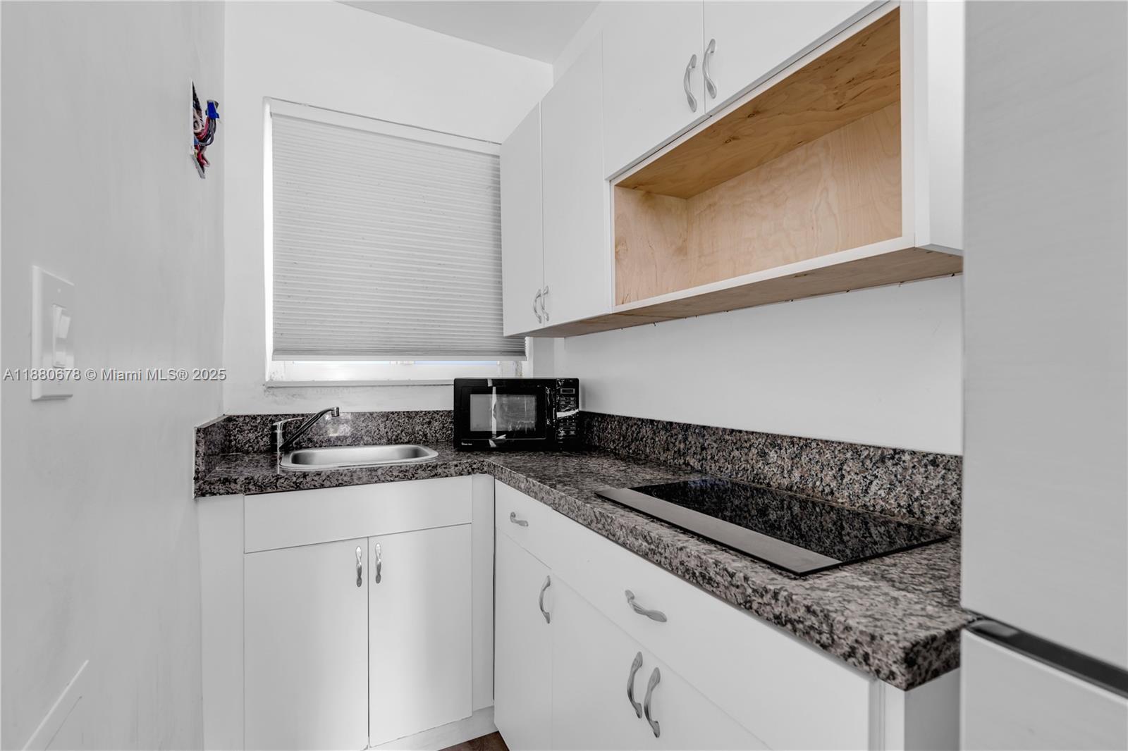 A small kitchen features white cabinets, granite countertops, a sink, and a built-in cooktop — 110 NW 9th Ave # 3, Miami FL 33128, MIAMI, FL