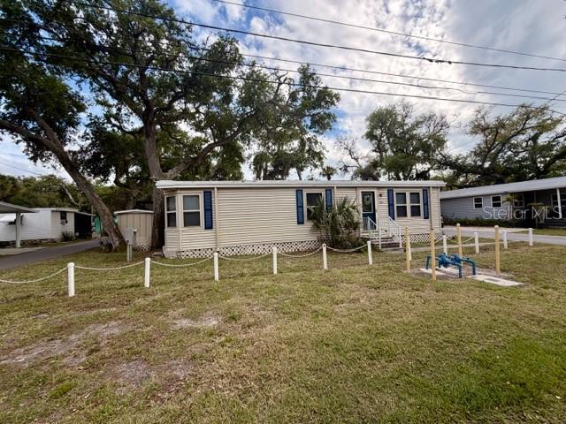 A single-story manufactured home with beige siding sits on a grassy lot with trees — 15010 113TH AVENUE N UNIT 53, LARGO, FL