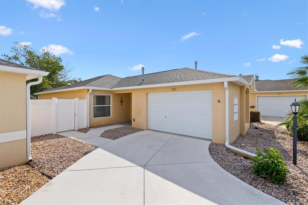 A tan, single-story house features a palm tree in the front yard and a driveway — 2117 SMOAKS STREET, THE VILLAGES, FL