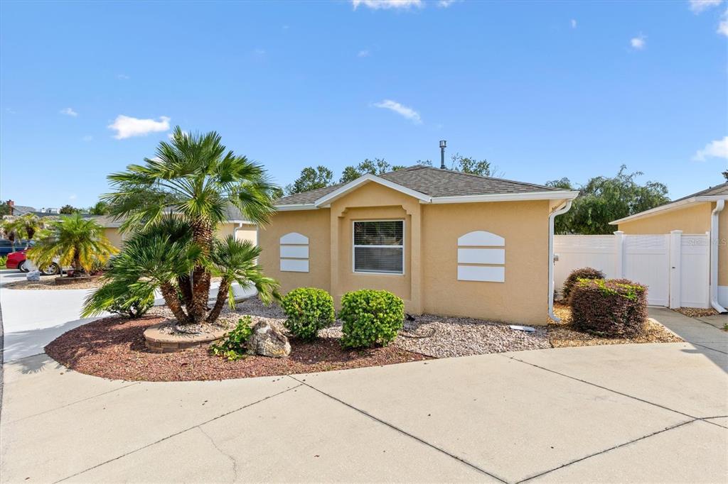 A single-story yellow house features a white garage door, a concrete driveway, and gravel landscaping — 2117 SMOAKS STREET, THE VILLAGES, FL