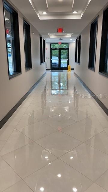 A long, brightly lit hallway features glossy white tile floors and dark-framed windows on both sides — 13550 VILLAGE PARK DRIVE UNIT GE, ORLANDO, FL